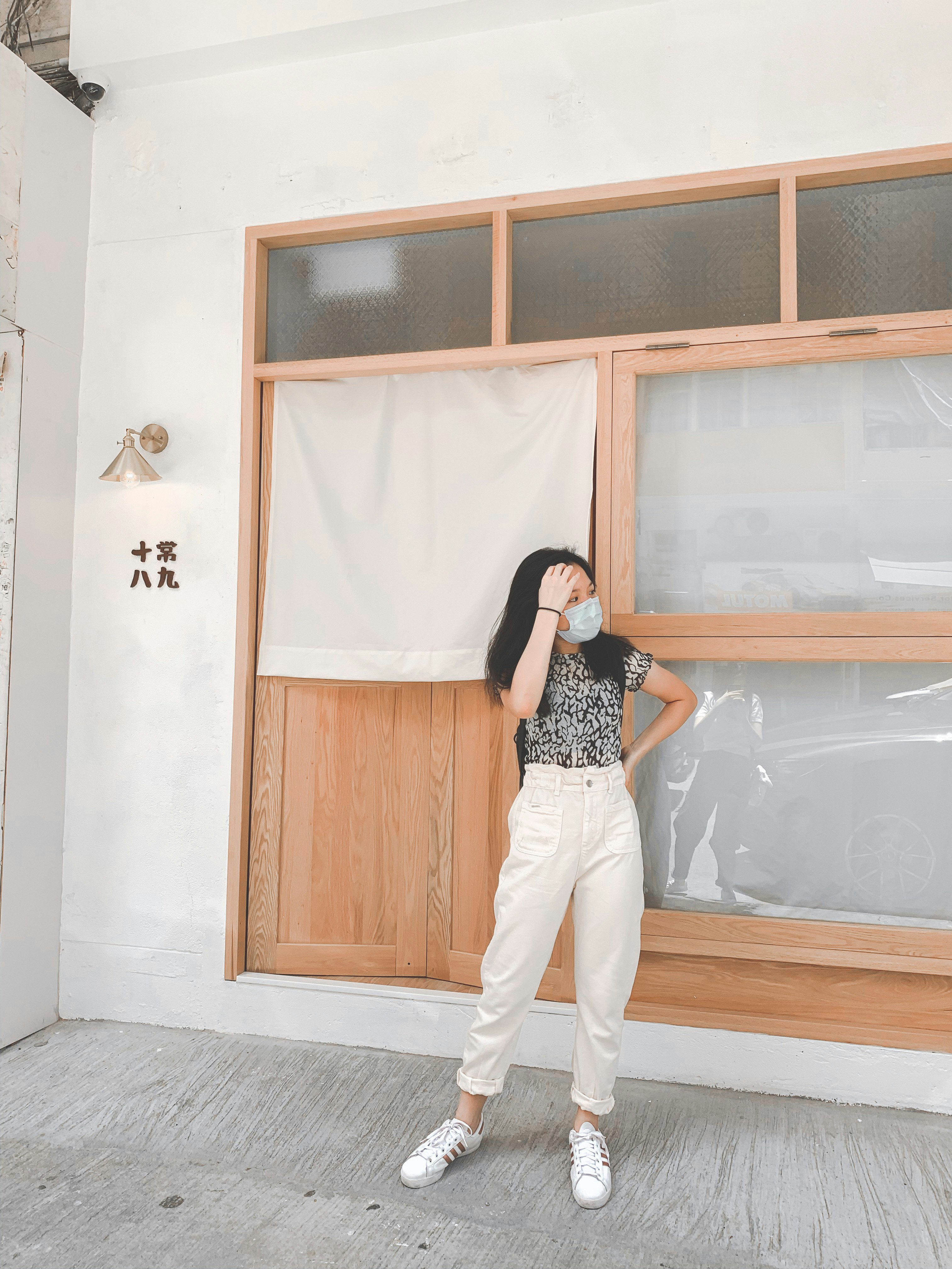 woman in black and white polka dot shirt and white pants standing beside brown wooden door